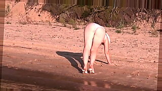 セクシーな日光浴をしたブロンドが海辺でストリップする。